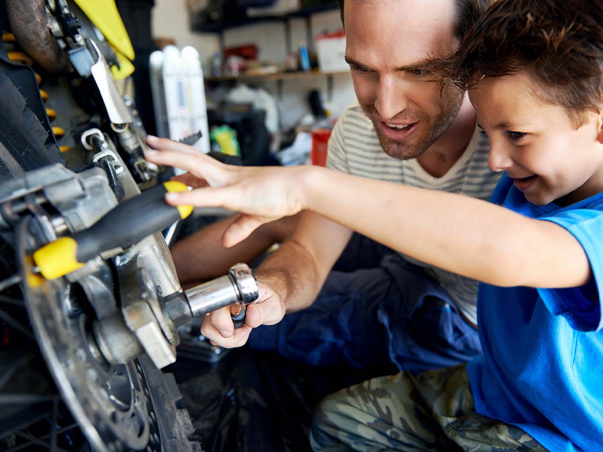 A boy helping his father work on a bike. 